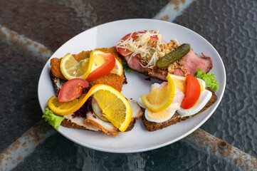 Open sandwiches bread with different kind of cold cuts on a plate standing on a rusty table