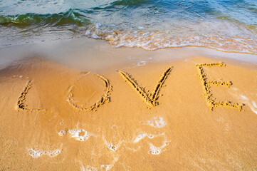 The word LOVE written on a yellow sandy shore near the sea