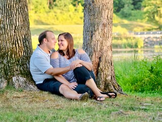 Fototapeta premium Couple in love and engaged sitting between two trees looking at each other with love and happiness in Keystone State Park in the Laurel Highlands of Pennsylvania at golden hour.