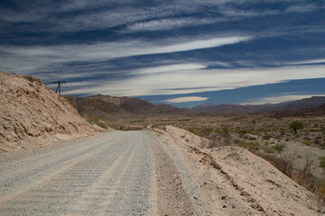 Fototapeta na wymiar Desert route 40 across the death valley in Salta, Argentina. View of the dirt road, desert and mountains under a beautiful blue sky with clouds.