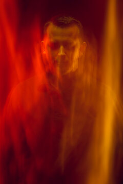 Mystical portrait of a young man in a photographic studio. Mixed light in red tones. Pulsed and continuous light.