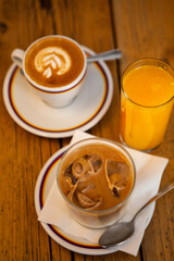 Two glasses and a cup with morning beverages (coffee - cappuccino, iced americano with milk, orange juice) on the wooden table in Florence, Tuscany, Italy. European breakfast