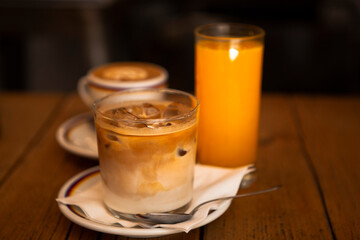 Two glasses and a cup with morning beverages (coffee - cappuccino, iced americano with milk, orange juice) on the wooden table in Florence, Tuscany, Italy. European breakfast