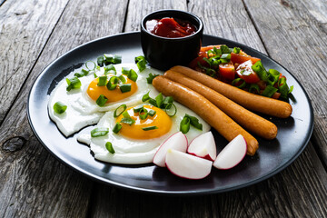 Breakfast - sunny side up egg, boiled sausages and vegetables served on wooden table
