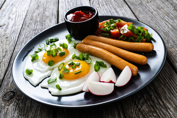 Breakfast - sunny side up egg, boiled sausages and vegetables served on wooden table
