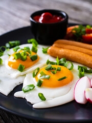Breakfast - sunny side up egg, boiled sausages and vegetables served on wooden table
