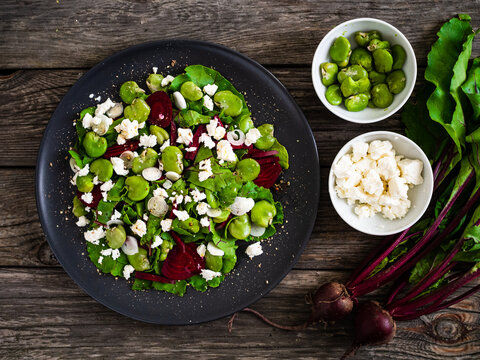Broad beans salad with beetroots, feta cheese, garlic and onion on wooden table
