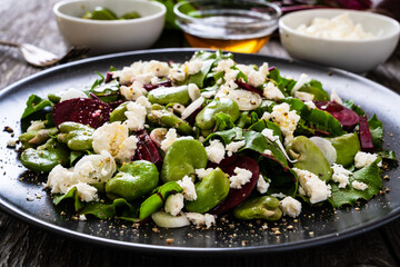 Broad beans salad with beetroots, feta cheese, garlic and onion on wooden table
