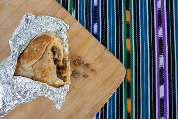 Carne Asada Burrito wrapped in foil, open with a bit taken out of it laying on a wooden board