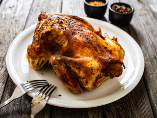 Whole roast chicken on on plate on wooden table
