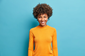 Half length shot of pretty cheerful young Afro American woman with nice beaming smile pleased...