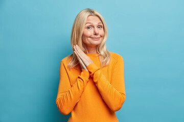 Tender positive middle aged woman clasps hands smiles happily hears something pleasant glad to meet...