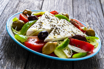 Fresh Greek salad - feta cheese, tomatoes, cucumber, red pepper, black olives and onion on wooden table
