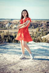 A girl in a red dress stands on the edge of a chalk cliff.