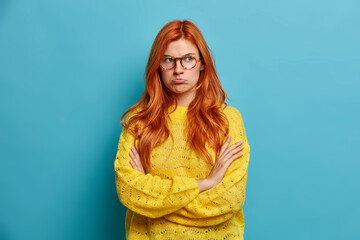 Portrait of sad offended redhead woman folds arms and purses lips sad after break up or quarrel...