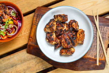 Plates of pan-Asian salad with sesame seeds and grilled chicken in pad thai sauce on wooden stands and loya chopsticks.