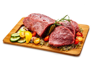 Fresh raw beef on cutting board with fresh vegetables on white background
