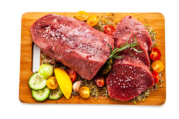 Fresh raw beef on cutting board with fresh vegetables on white background
