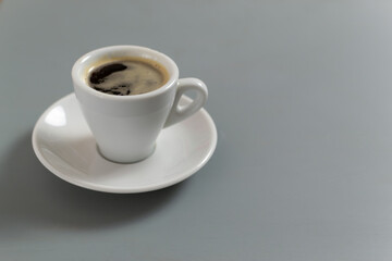 White cup with espresso coffee on a white saucer on a gray background. Selective focus. Copy space.