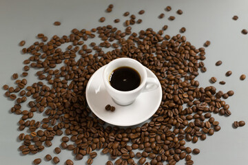 White cup with espresso on a white saucer among coffee beans on a gray background. Close-up....