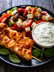 Fried souvlaki, greek salad and tzatziki on wooden table
