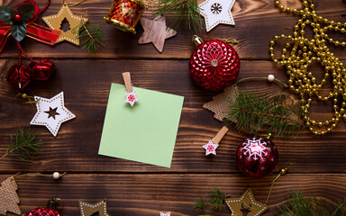 Christmas flat lay of red balloons and wooden stars and clothespins on a dark background with a square sheet for notes in the center. New year's frame, space for text. Xmas toys, beads, pine branches