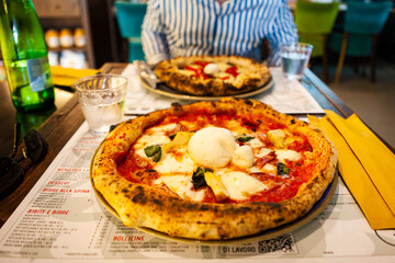 Delicious Italian pizza with mozzarella cheese, prosciutto, funghi (mushrooms) on the table at the local restaurant in the middle of Rome city, Lazio, Italy. European fast food and traditional dishes.