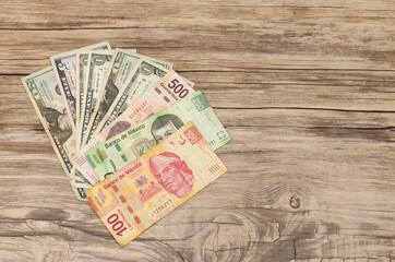 Dolares y pesos mexicanos sobre mesa de madera, aislados, con espacio en la mesa.