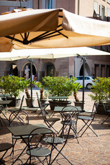 Close up urban view. Classic Italian street with restaurant tables, umbrellas and flowers in the city center with cars, vintage buildings in Bergamo, Lombardy, Italy. Antique European architecture.