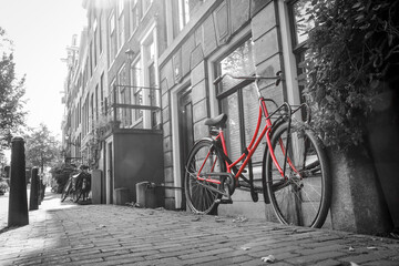 A picture of a lonely red bike on the street by the channel in Amsterdam. The background is black and white. 