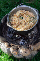 Rice with vegetables is cooked in a metal cauldron over the hearth