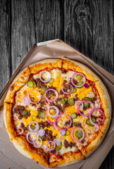 Pizza with Mozzarella cheese, Bolognese sauce, minced meat and vegetables. Italian pizza in paper box on wooden background.