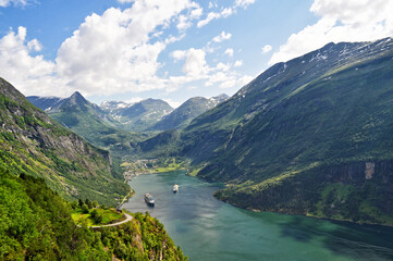 Fototapeta na wymiar High mountains and deep valley with small boats and the village of Geiranger fjord, Norway