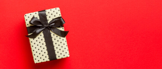 Top view Christmas present box with black bow on red background with copy space
