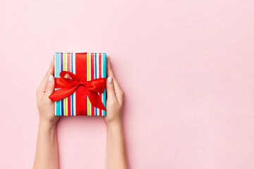 Female's hands holding striped gift box with colored ribbon on living coral background. Christmas...