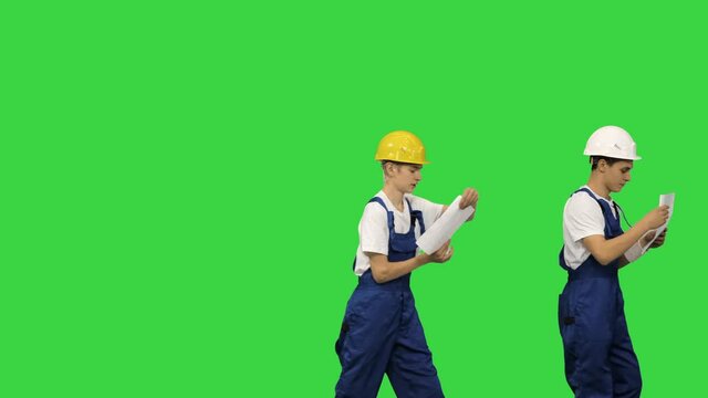 Three young construction workers in hardhats passing on documents while doing a silly walk in a row on a Green Screen, Chroma Key.