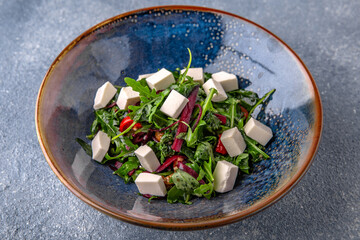 Arugula salad, cherry tomatoes, beets, olives and feta cheese. Natural delicious food. Greek cuisine menu. Still life in a marine style on a blue background.