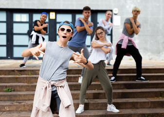 Happy positive teenagers learn dance movements at city street