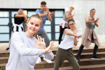 Portrait of emotional girl doing hip hop movements during group class at city street