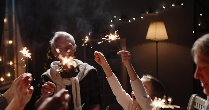 People celebrating christmas at home. Large caucasian family making a toast and clinking their glasses, holding bright sparklers and smiling - celebration concept 4k footage