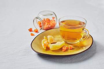 Delicious black tea in glass cup and candied fruits on yellow saucer