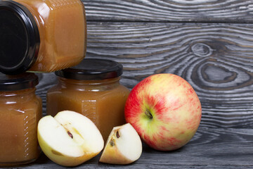 Apple jam in jars. Nearby are apple slices. On brushed boards, painted black and white.