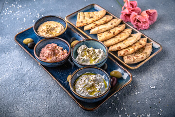 Assorted appetizers of cottage cheese with garlic, salmon with cheese, eggplant with pita. Natural delicious food. Greek cuisine menu. Still life in a marine style on a blue background.