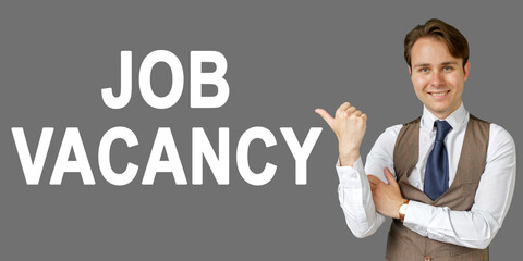 Emotional portrait of businessman showing right hand gesture on text - JOB VACANCY. Gray background.
