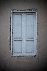 Tall white window closed with white shutters in a dark wall of an old building.