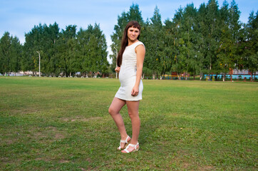 Happy pregnancy. Beautiful pregnant young woman in short white mini dress. Young woman in a green Park. Pregnancy 4 months. Girl in a dress and summer Sunny day.