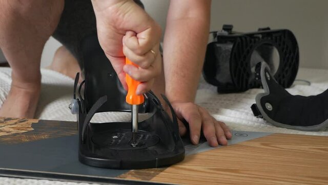 The man's hand attaches the bindings to the snowboard. Prepares the snowboard for winter