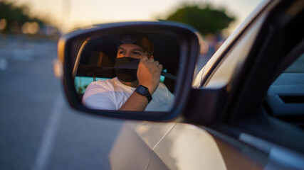 Fototapeta na wymiar Chico joven conduciendo su coche recien lavado y comprobando los espejos y cinturones usando mascarilla de la pandemia de coronavirus covid-19