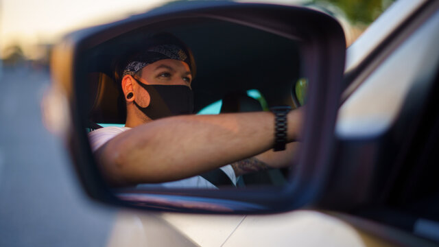 Chico joven conduciendo su coche recien lavado y comprobando los espejos y cinturones usando mascarilla de la pandemia de coronavirus covid-19