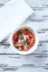 Simple salad with cherry tomatoes, red onion and fresh herbs. Bright wooden background. Top view.	